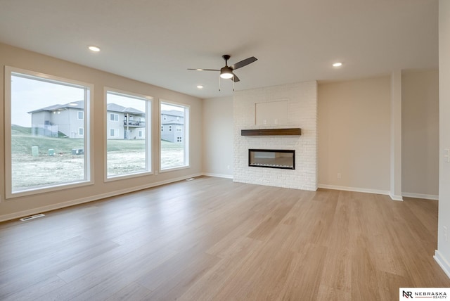 unfurnished living room with ceiling fan, light wood-type flooring, and a brick fireplace