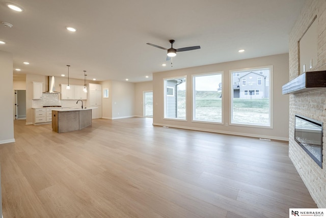 unfurnished living room featuring ceiling fan, sink, light hardwood / wood-style flooring, and a stone fireplace