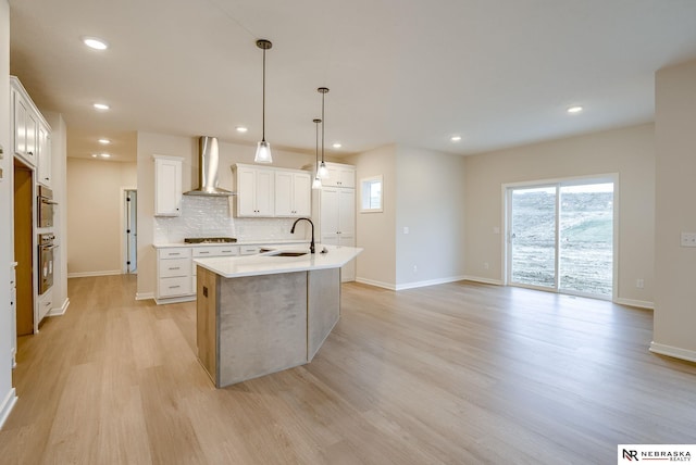 kitchen with black gas stovetop, pendant lighting, a center island with sink, white cabinets, and wall chimney exhaust hood