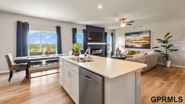 kitchen featuring a kitchen island with sink, a fireplace, dishwasher, white cabinets, and sink