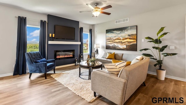 living room with a large fireplace, ceiling fan, a wealth of natural light, and hardwood / wood-style floors