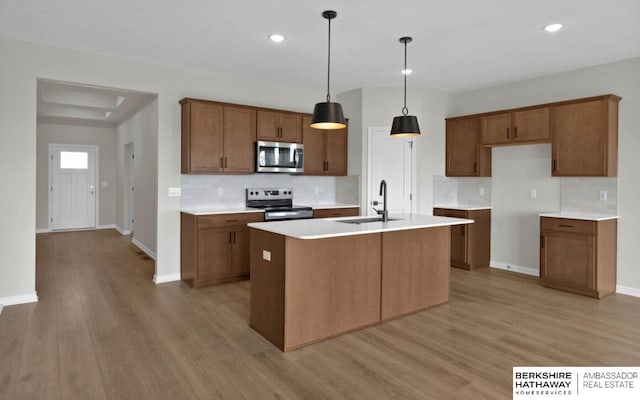 kitchen with stainless steel appliances, decorative light fixtures, a kitchen island with sink, light hardwood / wood-style flooring, and sink