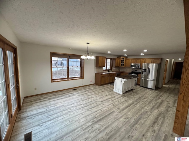 kitchen with light hardwood / wood-style flooring, an inviting chandelier, stainless steel appliances, a textured ceiling, and decorative light fixtures