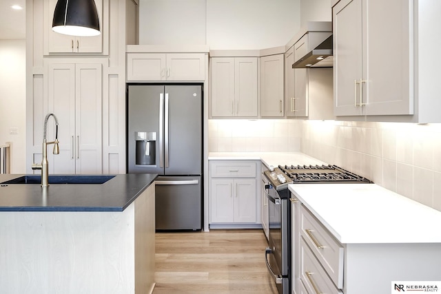 kitchen with appliances with stainless steel finishes, decorative backsplash, sink, hanging light fixtures, and light wood-type flooring