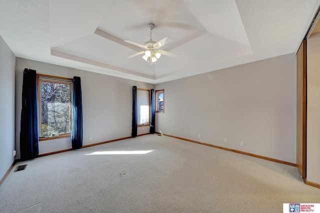 spare room with ceiling fan, light carpet, and a tray ceiling