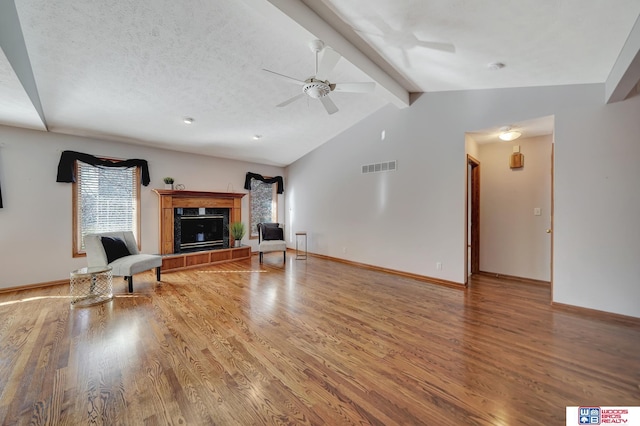 unfurnished living room with a textured ceiling, wood-type flooring, vaulted ceiling with beams, ceiling fan, and a tile fireplace