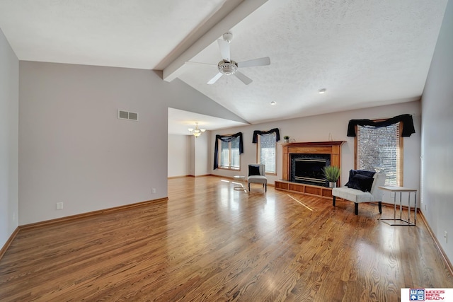 unfurnished living room with ceiling fan with notable chandelier, hardwood / wood-style floors, a textured ceiling, vaulted ceiling with beams, and a tile fireplace