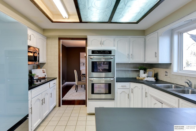 kitchen with sink, backsplash, white cabinets, light tile patterned floors, and stainless steel appliances