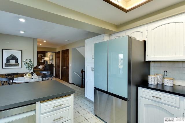 kitchen featuring backsplash, white cabinets, light tile patterned floors, and stainless steel refrigerator