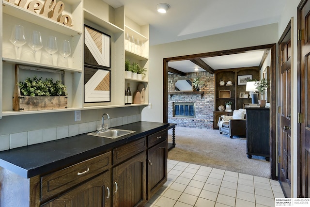 kitchen with light carpet, sink, built in features, a brick fireplace, and dark brown cabinetry