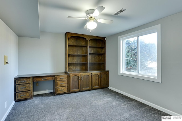 unfurnished office featuring built in desk, carpet, and ceiling fan