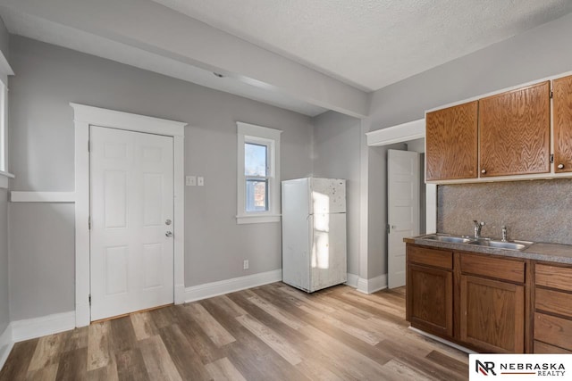 kitchen featuring a textured ceiling, white fridge, decorative backsplash, sink, and light wood-type flooring