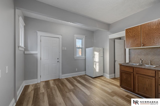 kitchen with light hardwood / wood-style flooring, sink, white refrigerator, a textured ceiling, and decorative backsplash