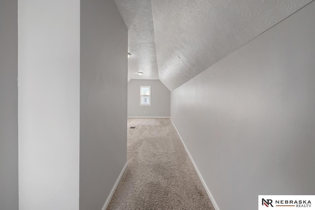 hall featuring a textured ceiling, light carpet, and vaulted ceiling