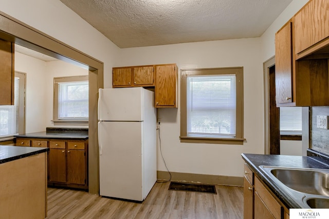 kitchen with sink, light wood-type flooring, white refrigerator, and a textured ceiling