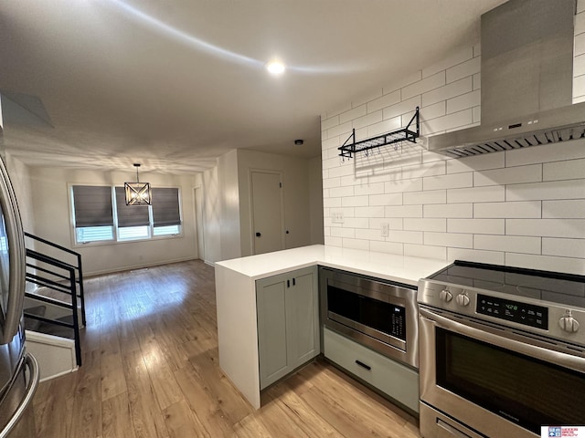 kitchen with light hardwood / wood-style floors, appliances with stainless steel finishes, gray cabinetry, backsplash, and wall chimney exhaust hood