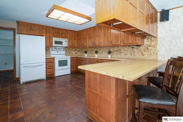 kitchen with kitchen peninsula, white appliances, tasteful backsplash, and a kitchen breakfast bar