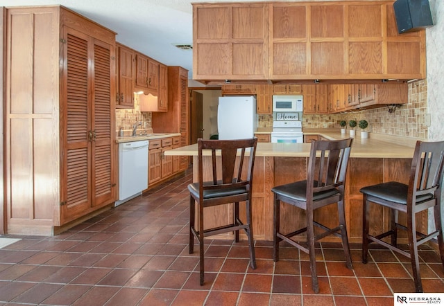 kitchen with decorative backsplash, white appliances, kitchen peninsula, and a breakfast bar area