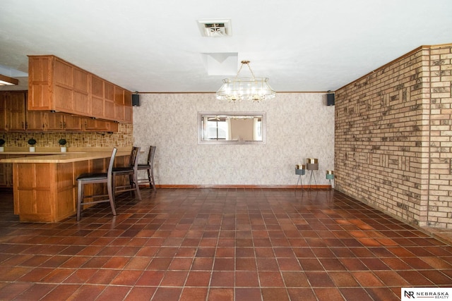 kitchen with kitchen peninsula, pendant lighting, brick wall, a chandelier, and a breakfast bar area