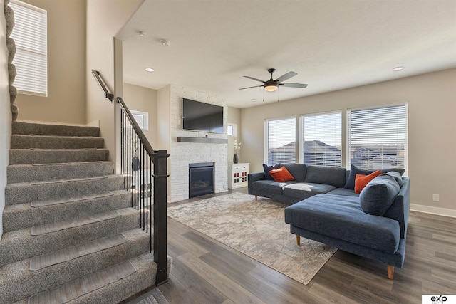 living room featuring a stone fireplace, dark hardwood / wood-style floors, and ceiling fan