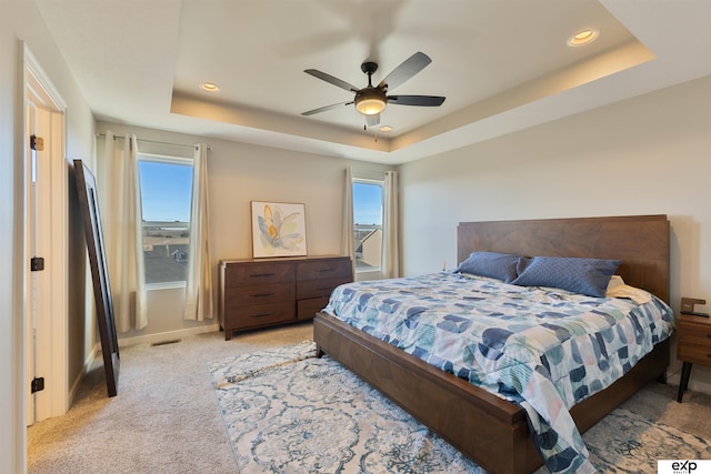 bedroom featuring a tray ceiling, light colored carpet, and ceiling fan