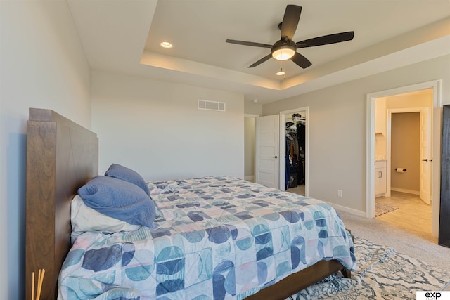 carpeted bedroom with ceiling fan, ensuite bathroom, a raised ceiling, a walk in closet, and a closet