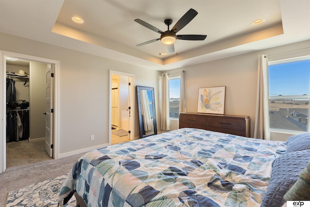 carpeted bedroom with a spacious closet, connected bathroom, ceiling fan, and a tray ceiling