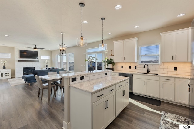 kitchen featuring a stone fireplace, pendant lighting, dishwasher, sink, and white cabinets