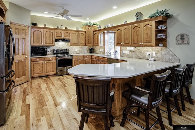 kitchen featuring black appliances, decorative backsplash, light hardwood / wood-style flooring, kitchen peninsula, and a breakfast bar area