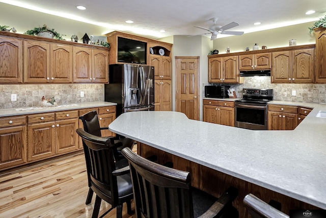 kitchen featuring exhaust hood, decorative backsplash, light wood-type flooring, a breakfast bar, and stainless steel appliances