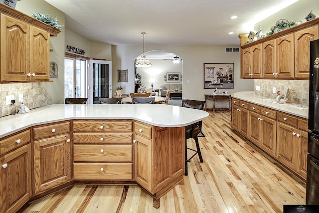 kitchen featuring light hardwood / wood-style floors, decorative backsplash, pendant lighting, a breakfast bar, and ceiling fan