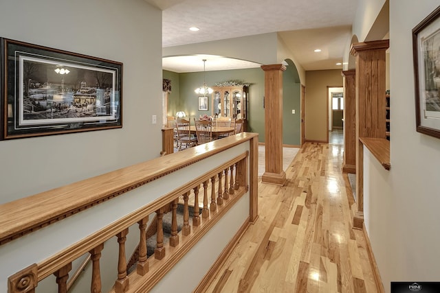 corridor with light wood-type flooring, an inviting chandelier, and ornate columns