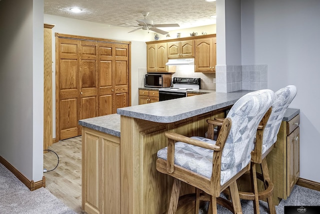 kitchen featuring kitchen peninsula, backsplash, light hardwood / wood-style floors, a kitchen bar, and black appliances