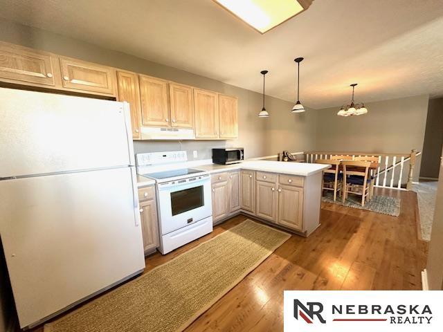 kitchen with white appliances, decorative light fixtures, kitchen peninsula, a chandelier, and light wood-type flooring