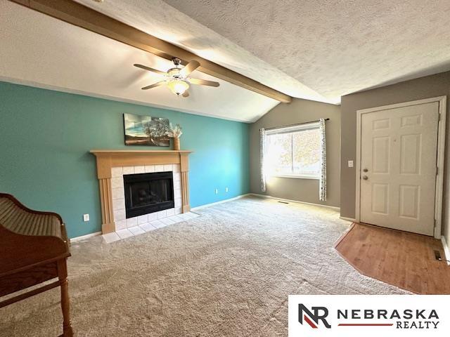 carpeted living room featuring lofted ceiling with beams, a tile fireplace, a textured ceiling, and ceiling fan