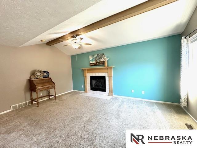 unfurnished living room with ceiling fan, carpet, a fireplace, a textured ceiling, and vaulted ceiling with beams