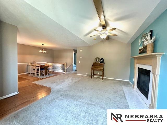 unfurnished living room with ceiling fan with notable chandelier, carpet, and vaulted ceiling with beams