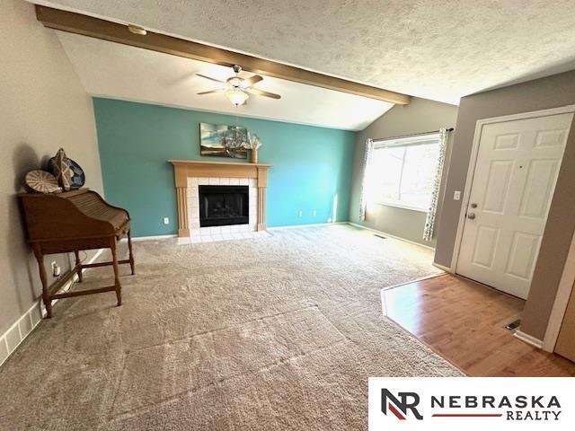 living room featuring ceiling fan, a tiled fireplace, a textured ceiling, vaulted ceiling with beams, and carpet floors