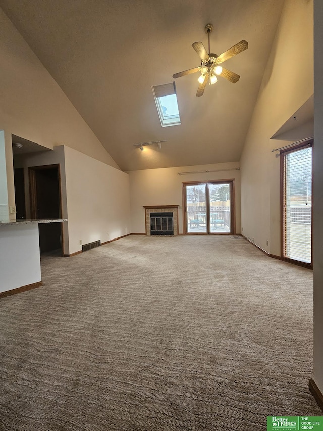 unfurnished living room featuring a skylight, a fireplace, high vaulted ceiling, and carpet flooring