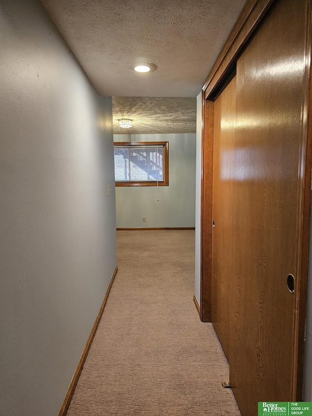 hallway featuring light colored carpet and a textured ceiling