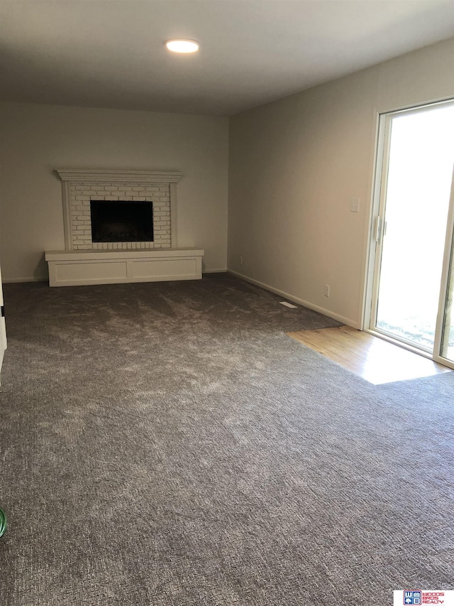 unfurnished living room featuring dark colored carpet, a wealth of natural light, and a fireplace