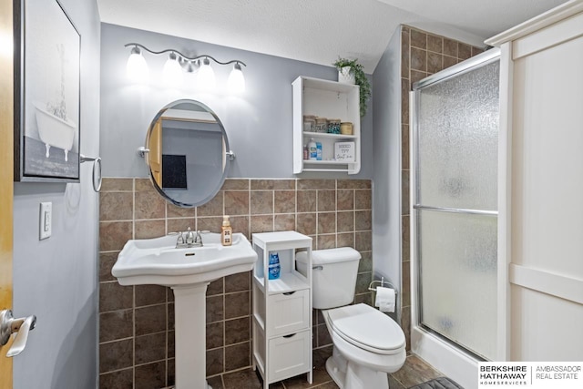 bathroom with tile walls, toilet, a shower with door, and a textured ceiling