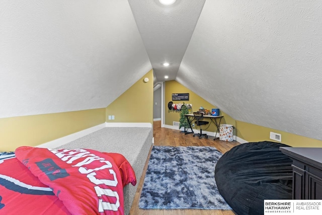 bedroom with a textured ceiling, hardwood / wood-style floors, and vaulted ceiling