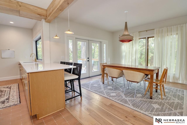 dining space with sink, beamed ceiling, french doors, and light hardwood / wood-style flooring