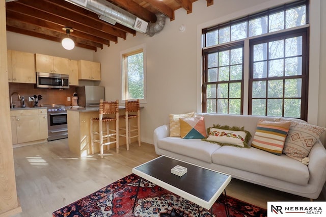 living room featuring sink, light hardwood / wood-style flooring, and beamed ceiling