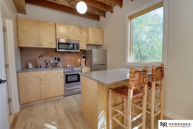 kitchen with appliances with stainless steel finishes, light brown cabinets, beamed ceiling, sink, and a breakfast bar