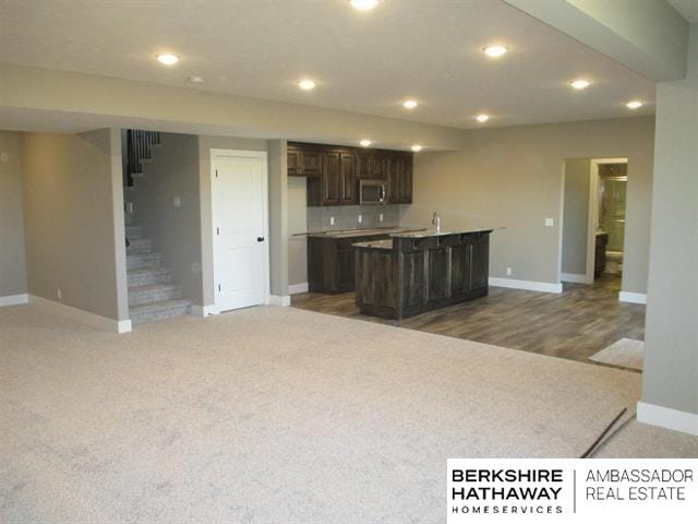 kitchen featuring dark brown cabinets, backsplash, a kitchen island with sink, and carpet floors