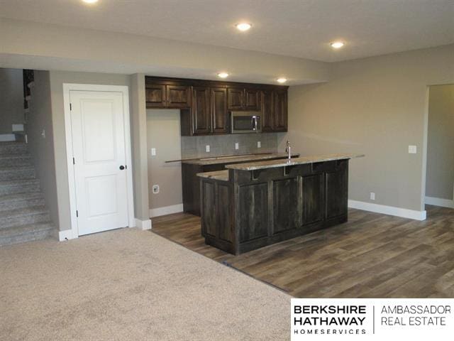 kitchen featuring sink, dark brown cabinets, backsplash, and a kitchen island with sink