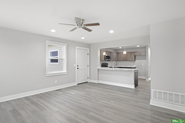 unfurnished living room featuring light hardwood / wood-style floors, sink, and ceiling fan