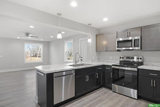 kitchen featuring appliances with stainless steel finishes, hanging light fixtures, sink, light wood-type flooring, and kitchen peninsula